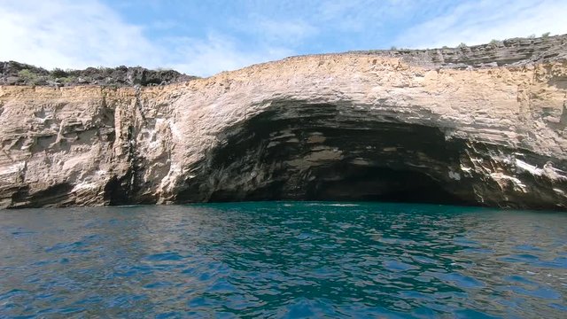 Beautiful natural rock arch, on cliff edge shoreline. Caves boat trip. Orange rock with green and blue ocean background. Shot on expedition off Isabela island, Galapagos, Ecuador.