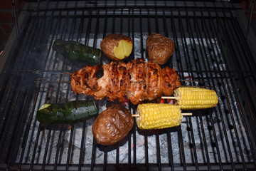 Courgettes, potatoes, sweet corn on the cob and chicken meat on the British barbecue. Grilled meat and vegetables cooked outdoors. Willesden Green, London, UK
