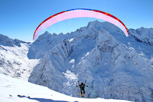 paraplane flying over snowy Caucasus mountains sunny blue sky