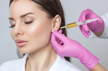 Cosmetologist does prp therapy for smoothing wrinkles and against flabbiness of skin on earlobe of...