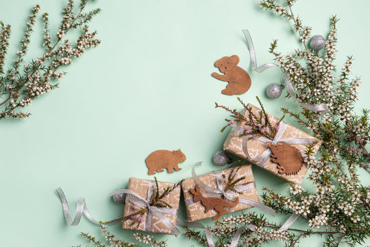 Australian inspired Christmas background with decorations, branches and gifts. Australian native tea tree foliage decorated with cute mammal decorates such as wombat, echidna, kangaroo and koala. 