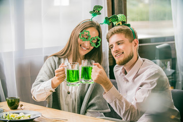 The company of young people celebrate St. Patrick's Day. They have fun at the bar. They are dressed in carnival headgear