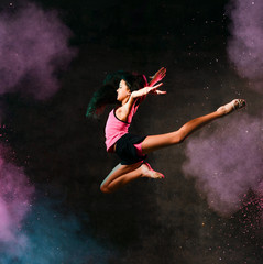 Fototapeta na wymiar Street dance girl dancer jumping up dancing in neon light doing gymnastic exercises in studio on dark wall