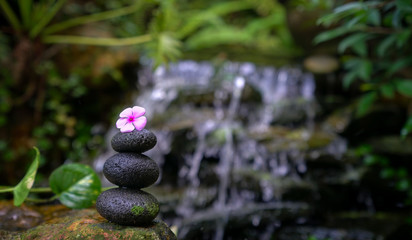 Obraz na płótnie Canvas Stack of zen stones with a pink flower on top. Nature with waterfall background.
