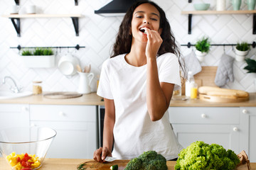 Pretty young african girl cooking eating a cucumber