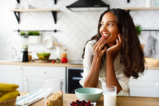 Pretty african girl has dreamy look and eats a raspberry before a breakfast