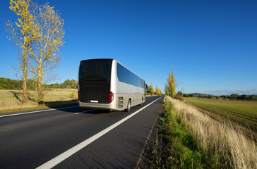 Bus driving on asphalt road in autumn rural landscape