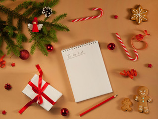 Fototapeta na wymiar Christmas composition. Notepad, pencil, spruce branches, gift box, candy canes, gingerbread and balls on a beige background. Winter, New year.