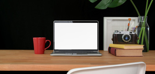 Cropped shot of trendy workspace with blank screen laptop computer and office supplies on wooden table