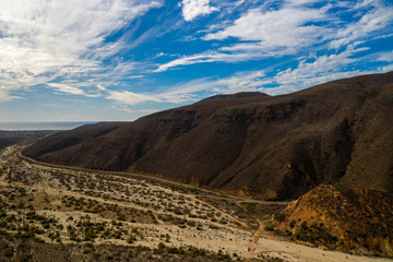 Fototapeta na wymiar Aerial Drone shot of coast and mountains in Baja, Mexico with a beautifully lit sky and clouds as well as the mountains leading up to the coast.