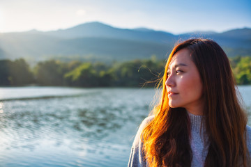 Portrait image of a beautiful asian woman standing in front of the lake and mountains before sunset