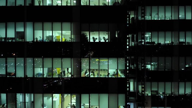 Aerial view of the  skyscraper windows at night with a lot of office people inside, who works overtime