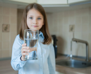 Little child is drinking clean water at home, close up. Caucasian cute girl with long hair is holding a water glass in her hands. Taking care of own health. Concept  of healthy lifestyle, good  habit