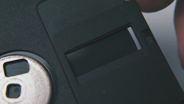 young man pushes cap of vintage diskette in black plastic case on clean white background extreme close view