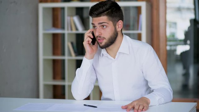 angry stressed out man talking on the phone with business clients wearing white shirt in modern company office