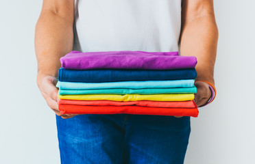 close up stack of folded multicolored t-shirt in hands over white background, copy space