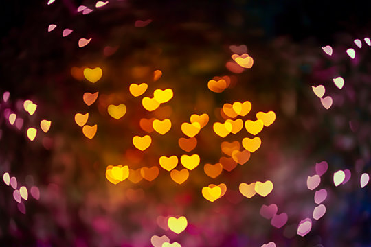 Abstract beautiful blurred gold-yellow orange and red colored of heart bokeh like autumn leaves from ornamental lights flickering in the park. Background for Autumn season, Valentine or Love concept.