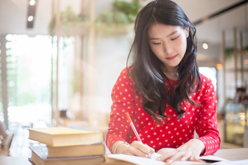 Young beautiful Asian woman reading a book while doing her homework in the modern co working space