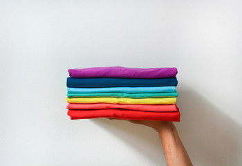 close up stack of folded multicolored t-shirt in hand over white background, copy space