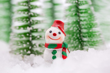 Happy snowman on snow with background of blurred Christmas pine. Miniature people in Christmas Theme.