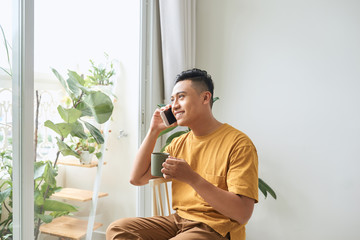 Young man wearing casual clothes talking on a mobile phone in the morning at a window - Powered by Adobe