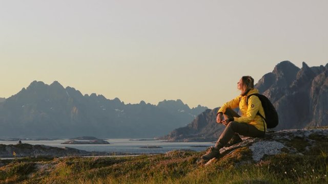 Woman traveler relaxing and enjoying the view of a Norwegian landscape from a hill. Adventure backpack traveling to Norway.