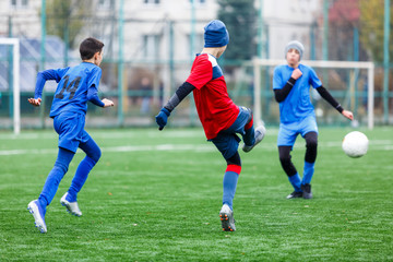 Obraz premium Boys in red and blue sportswear plays football on field, dribbles ball. Young soccer players with ball on green grass. Training, football, active lifestyle for kids concept