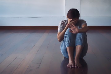 A young woman suffering from depression Sitting on the wooden floor in the room alone.