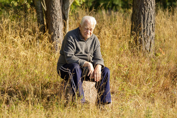 Naklejka na ściany i meble Gray-haired old man sitting on big stone outdoors.