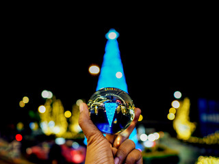 hand holding crystal ball with Christmas city light decoration on street reflection.
