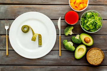 Diet program concept. Empty plate, measure tape and vegetables on dark wooden background top view