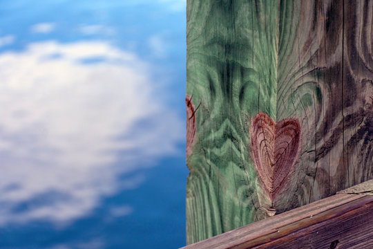 A wood knot in the shape of a heart, on a pier with sky reflected on water in the low country, South Carolina.