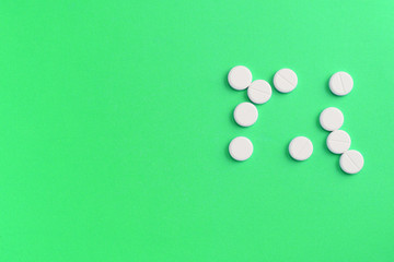 White pills scattered on a green surface. Top view, copy space. Medical background