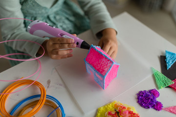 Cute little girl makes a plastic house, draws parts with a 3D pen. STEM and STEAM education. Development, modeling, education, design with hot plastic. Modern technologies. DIY.