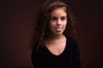Naklejka premium baby girl on dark background in warm colors with long curly hair curls. Looks away from the lens