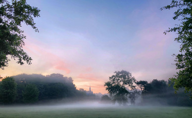 Colorful glowing sunrise with mist over a countryside meadow area around a distant castle, creating an idyllic scenic landscape
