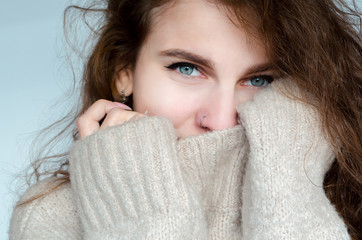 Winter portrait of a beautiful curly woman with blue eyes in a warm sweater with a pierced nose.