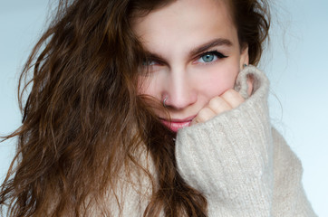 Winter portrait of a beautiful curly woman with blue eyes in a warm sweater with a pierced nose.