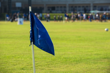 Blue corner flag from a football pitch, seeing group of players, coach, staffs and parents walking...
