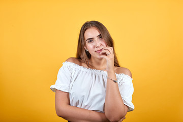 Attractive young woman keeping finger on mouth, looking pretty isolated on orange background in studio in casual white shirt. People sincere emotions, lifestyle concept.