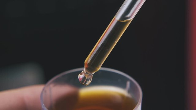 lab assistant takes brown liquid with glass pipette from cup on dark background extreme close view
