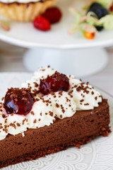 Chocolate cake with whipped cream decorated with cherries in a sweet sauce.