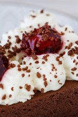 Chocolate cake with whipped cream decorated with cherries in a sweet sauce.