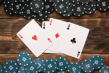 Poker chips and four aces cards on wooden table background.