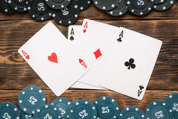 Poker chips and four aces cards on wooden table background.