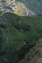 Anonymous tourist sitting on coast of lake and delighting in view of powerful mountain