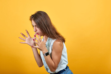 Angry caucasian young woman spreads hands isolated on orange background in studio in blue denim...