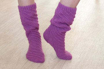 Female legs in high knitted socks of violet color on a beige background