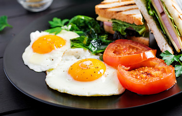 Breakfast: fried egg, spinach, tomatoes and club sandwich on plate.