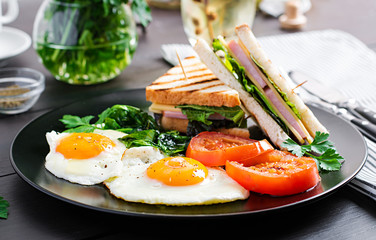 Breakfast: fried egg, spinach, tomatoes and club sandwich on plate.